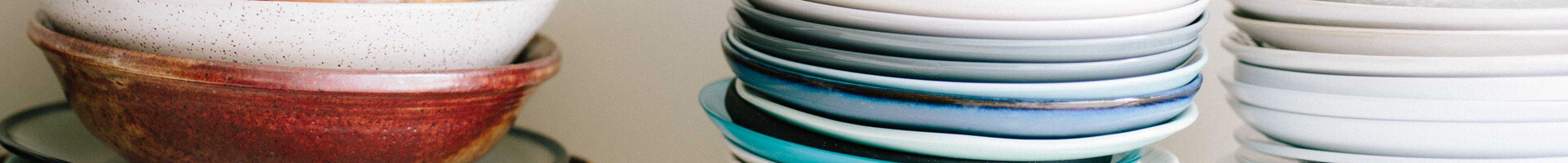 Several stacks of plates in different colors on a shelf.