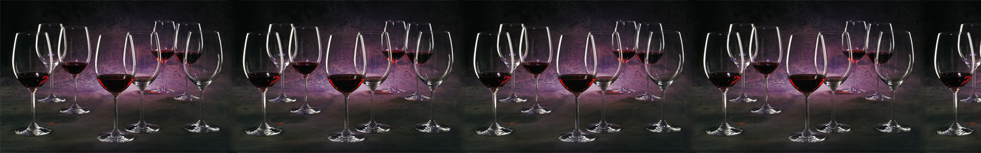 Numerous wine glasses from the Riedel Wine series are filled with red wine and stand in violet light.