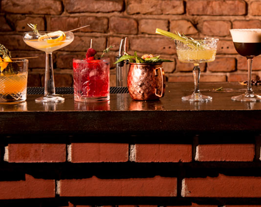 Cocktail glasses from Barstuff with colorful cocktail creations stand in a row on the bar.