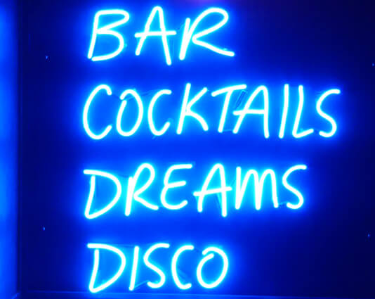 Blue neon sign with the words bar, cocktails, dreams, disco.