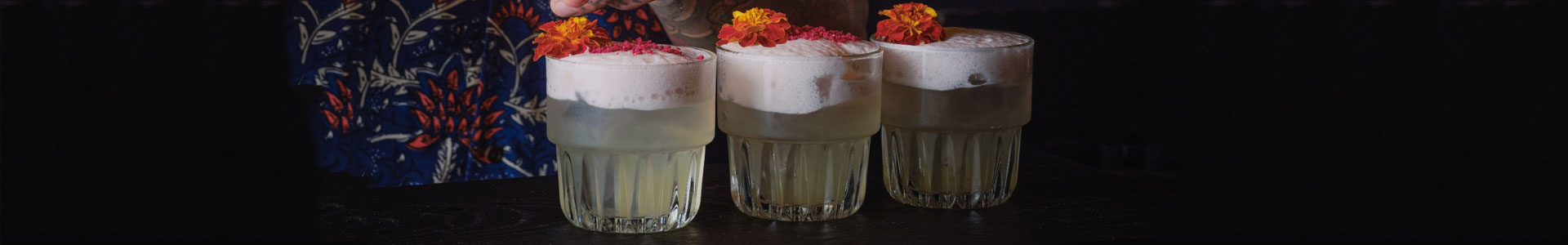 Three identical small tumblers from the Everst series by Libbey, filled with a light-colored drink with a frothy top and each garnished with an orange-red blossom.