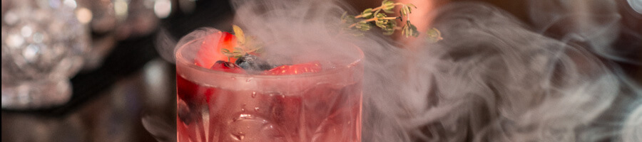 A red drink in a tumbler surrounded by puffs of light smoke.