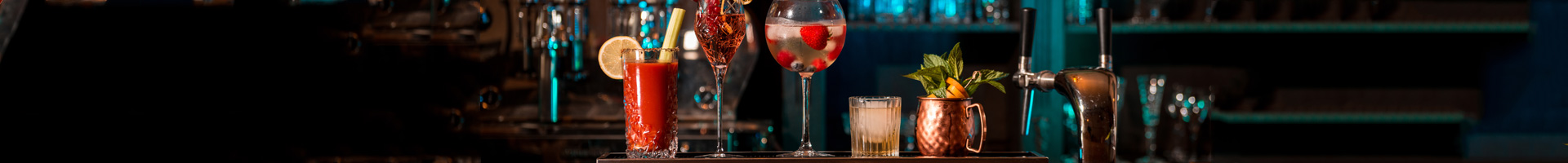 Cocktail glasses from Barstuff with colorful cocktail creations stand in a row on the bar.