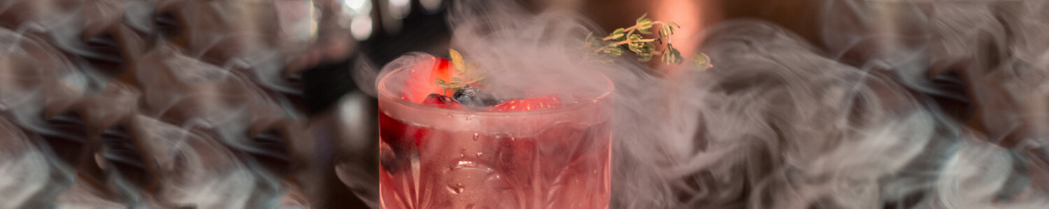 A red drink in a tumbler surrounded by puffs of light smoke.