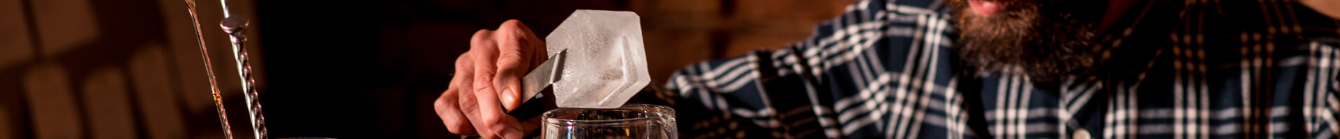 A bartender holds a large ice cube with ice tongs.