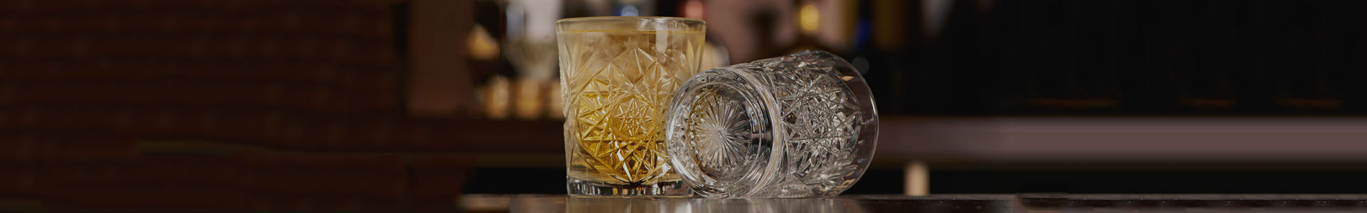 Two tumbler glasses from the Onis Hobstar series. One is standing, the bottom of the other is visible. The sides and base are decorated with an embossed pattern.
