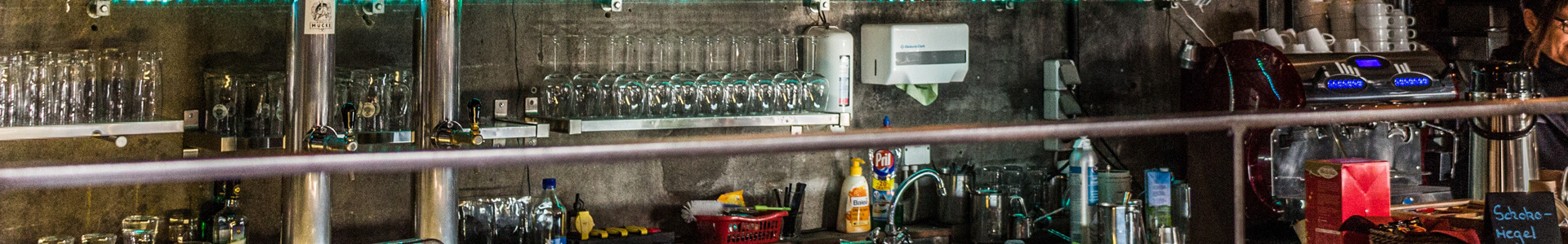 Glasses, sink and dishes behind the counter of a bar.