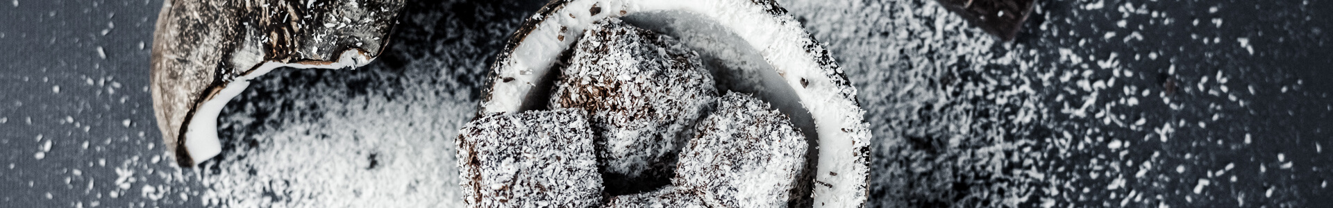 Coconut halves, shredded coconut and chocolate scattered over a black plate.